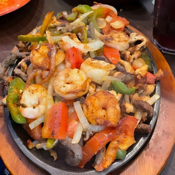 Sizzling shrimp and beef fajitas with colorful bell peppers and onions on a hot skillet.