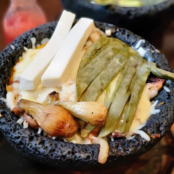El Agave Mexican Grill's molcajete with melted cheese, nopales, and grilled onions in a dark stone bowl.