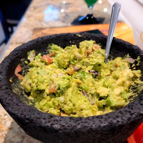 Freshly made guacamole with tomatoes and onions in a dark, textured bowl with a spoon.