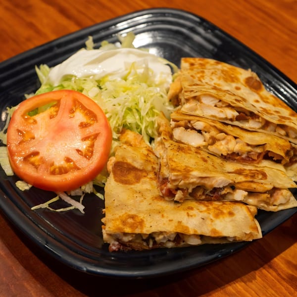 Chicken quesadillas with shredded lettuce, a tomato slice, and sour cream on a black plate.