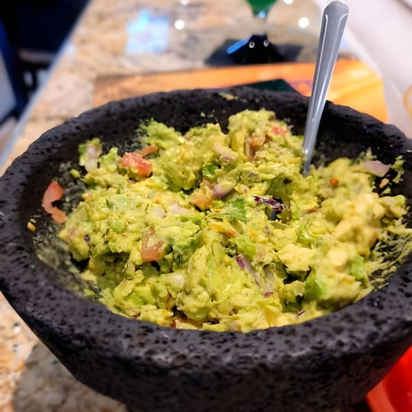 Freshly made guacamole with tomatoes and onions in a dark stone molcajete at El Agave Mexican Grill.