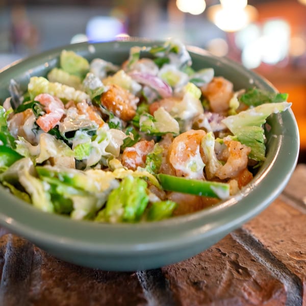 A close-up of a vibrant shrimp salad with lettuce, red onions, and creamy dressing in a green bowl.