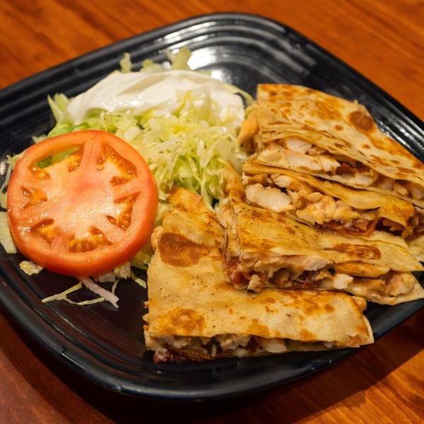 Chicken quesadillas with shredded lettuce, a tomato slice, and sour cream on a black plate.