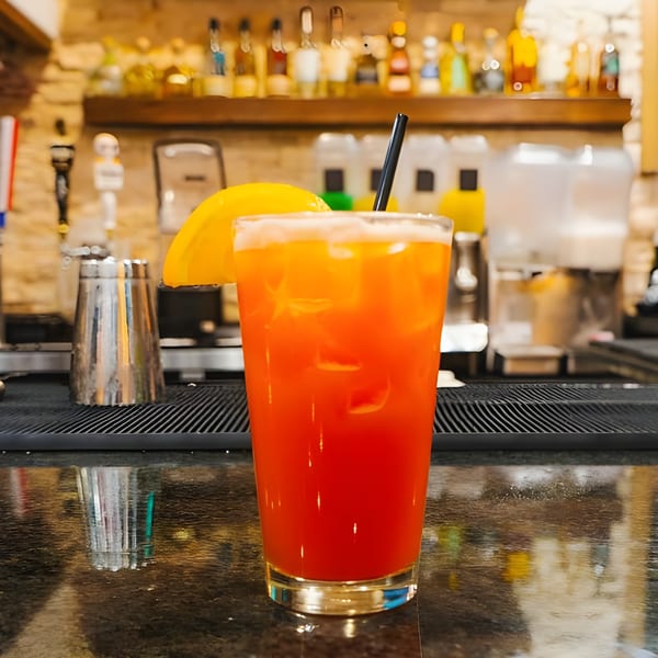 A vibrant orange and red cocktail with a lemon slice and black straw on a bar counter.