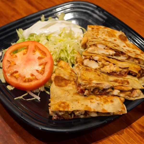 Chicken quesadillas with shredded lettuce, a tomato slice, and sour cream on a black plate.