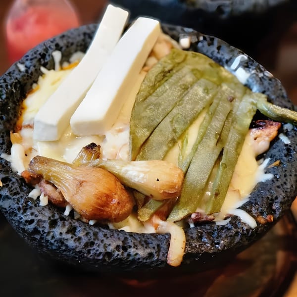 Molcajete dish with melted cheese, grilled nopales, and spring onions in a dark stone bowl.