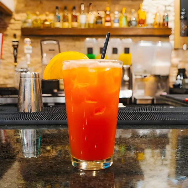 A vibrant orange and red Mexican cocktail with a lemon slice and straw on a bar.