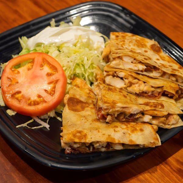 Chicken quesadillas with melted cheese, served with shredded lettuce, a tomato slice, and sour cream.
