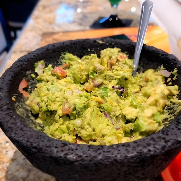 Fresh guacamole with diced tomatoes and onions in a dark, textured molcajete with a spoon.