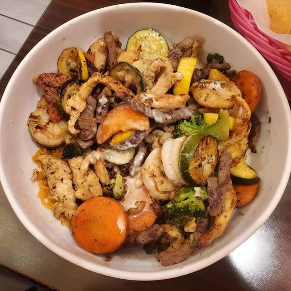 A white bowl filled with grilled chicken, steak, shrimp, and mixed vegetables with a creamy sauce.