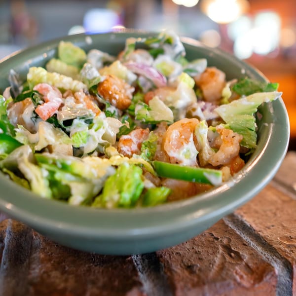 A vibrant shrimp salad with lettuce, red onion, and creamy dressing in a green bowl.