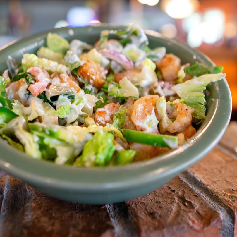 A vibrant shrimp salad with lettuce, red onion, and creamy dressing in a green bowl.
