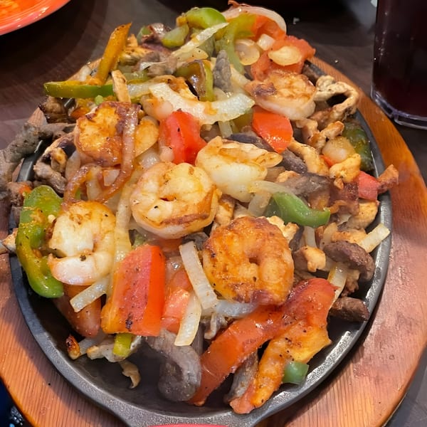 Sizzling fajitas with shrimp, steak, bell peppers, and onions on a hot skillet from El Agave Mexican Grill.