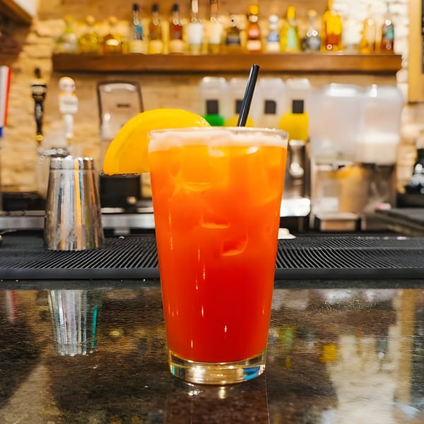 A vibrant orange and red cocktail with a lemon slice and black straw on a bar.